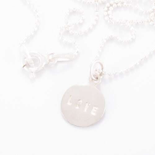 Our Fine Sterling Silver Small Love Disc Necklace. Shown here, in stunning 925 sterling and stamped "LOVE". In short, this petite piece is sure to give lots of love. The perfect gift for someone special or as a self-indulgent addition to any jewelry collection.