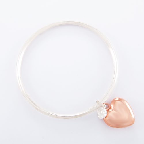 Our Sterling Silver Bangle with Rose Gold Puffed Heart. Shown here, with a handcrafted band with a bevel-edge and pink gold over a large 925 sterling puffed heart. As well as, with a small sterling heart. It’s a truly stunning and unique piece. In short, the perfect gift idea, with twice the love. Or as a self-indulgent purchase to add to your own jewelry collection.